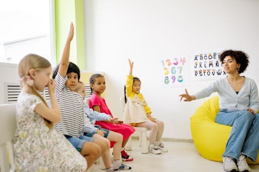 Children raising hands in classroom with a teacher, learning and engaging.