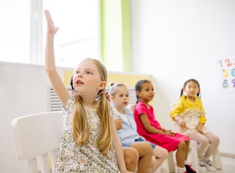 Kindergarten students in a classroom raising hands to participate in learning activities.