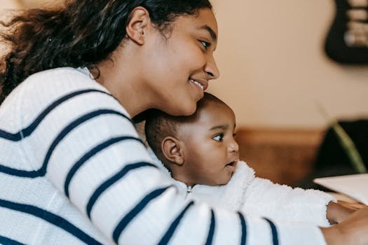 Side view of positive ethnic mother with curious toddler spending time at table in light room while looking away
