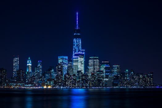 Illuminated New York City skyline reflecting over the Hudson River at night.