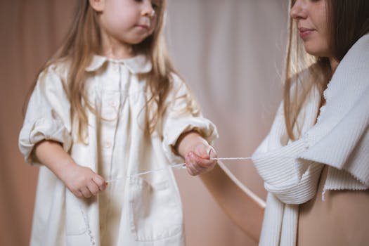 A mother and daughter playfully interacting with yarn indoors, capturing a tender family moment.