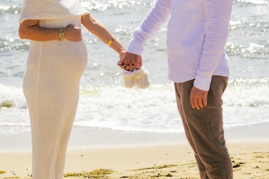 Pregnant couple holding baby shoes on a sunny beach in Balıkesir, Türkiye.