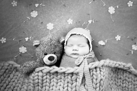 Adorable newborn baby sleeping with a teddy bear, wrapped in a cozy blanket in a black and white setting.