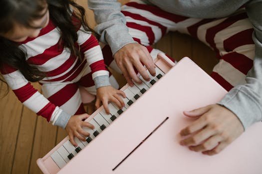 A child and adult play a toy piano in matching striped pajamas, creating a family moment.