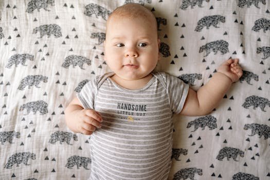 Cute baby boy wearing a striped onesie, lying on a bear-patterned blanket with a smile.