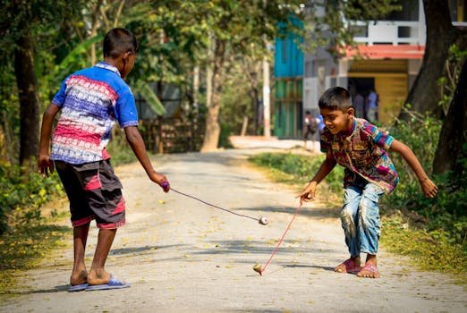 Two boys joyfully play with spinning tops on a sunlit rural path.