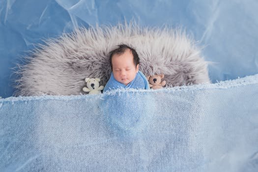 A cute newborn baby peacefully sleeps in a blue blanket with teddy bears.
