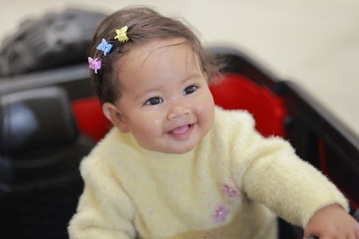 Adorable baby with colorful hair clips in a yellow sweater, smiling joyfully indoors.