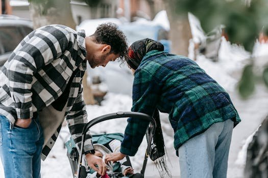 Side view of ethnic couple wearing casual clothes adjusting clothes on baby lying in stroller during stroll in winter street