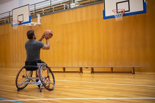 An adult male player in a wheelchair shooting basketball indoors, showing inclusivity in sports.