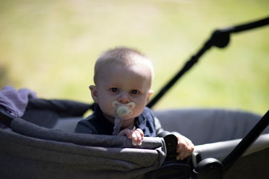Adorable baby sitting in stroller outdoors with a pacifier, enjoying a sunny day in the park.