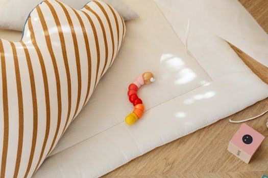 A small colorful toy worm placed on a wooden floor with striped pillow and soft play mat.
