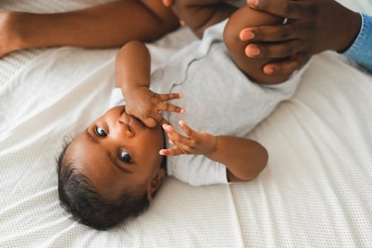 Cute baby in a onesie lying on a bed with parent's hands nearby, creating a warm and loving atmosphere.