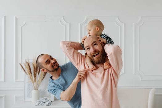 A heartwarming scene of a baby enjoying playful time with loving same-sex parents indoors.