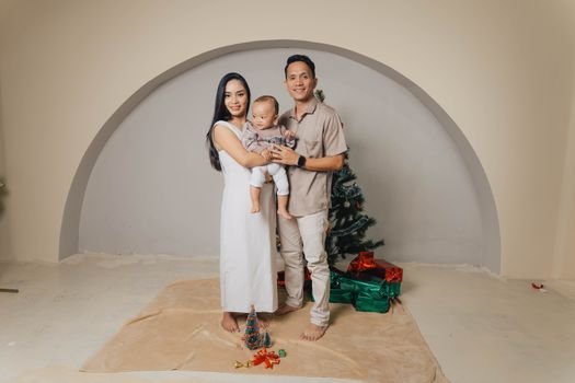 Happy family posing indoors with Christmas tree and gifts.