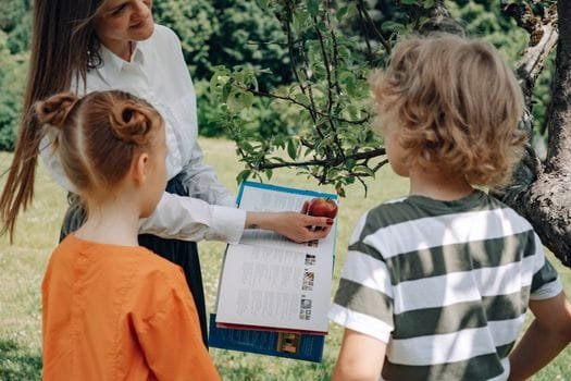 A woman teaching children about apples in a garden, engaging in outdoor education.