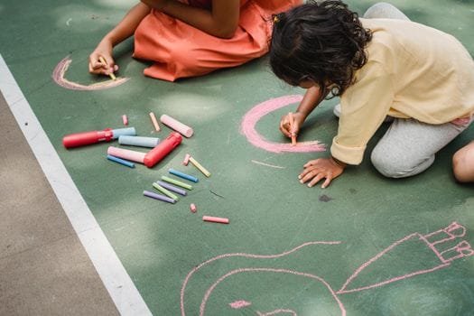 Two kids drawing with colorful chalk on pavement, expressing creativity and enjoying outdoor play.