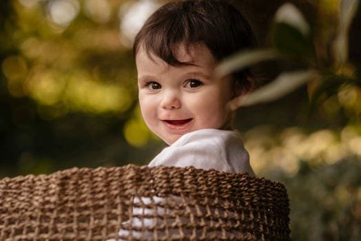 Charming portrait of a smiling baby outdoors in a woven basket, surrounded by nature.
