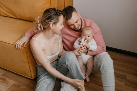 A happy family with their baby smiling and sitting on a sofa in a cozy living room.