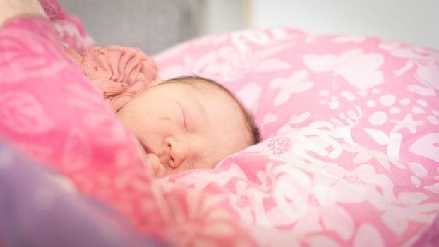 Close-up of a baby peacefully sleeping on a pink floral blanket indoors during the day.