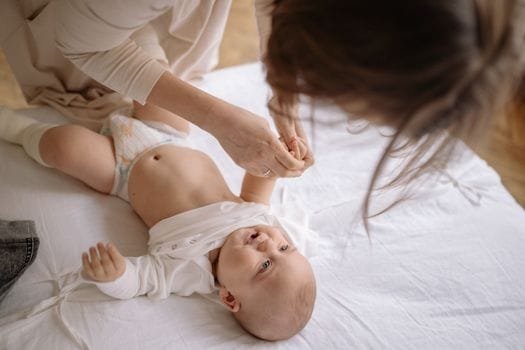 Mother gently changes baby's onesie in a cozy home setting, nurturing and caring bond.