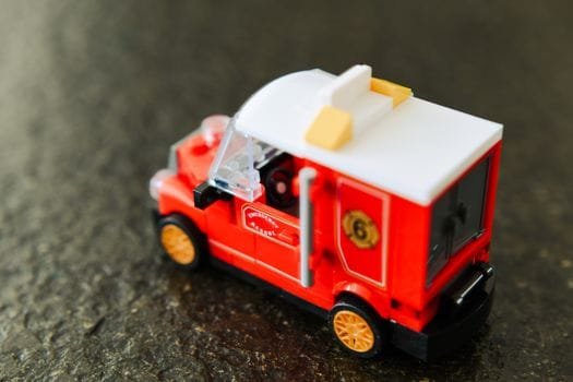 Detailed close-up of a red toy van on a textured dark surface, showcasing intricate design.