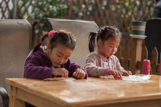 Two young girls engaged in a creative art project outdoors, emphasizing concentration and creativity.