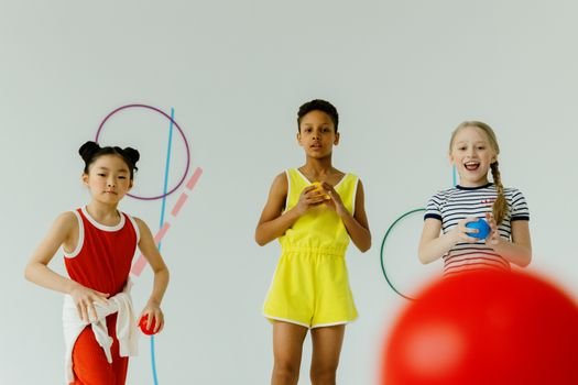 Three diverse children having fun playing with colorful balls indoors, promoting creativity and togetherness.