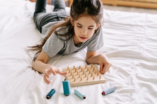 Girl plays with a geoboard and threads, fostering creativity and mindful learning.