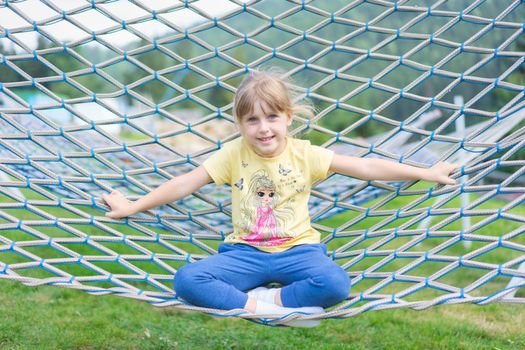 Caucasian girl sitting on a hammock outdoors, smiling and enjoying a sunny day.