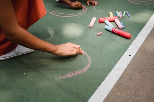 Children using colorful chalk to draw on outdoor playground surface, capturing a joyful creative moment.