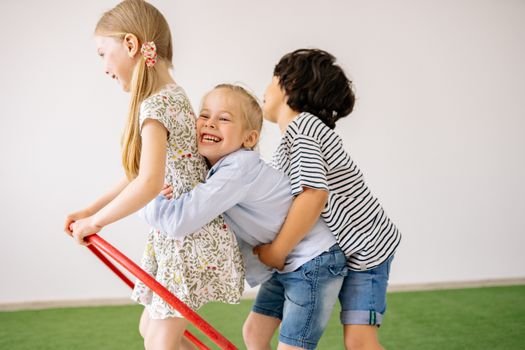 Three children joyfully play indoors with a hula hoop, showcasing happiness and togetherness.