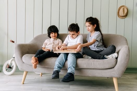 Three children playing together on a couch indoors, enjoying their time with a board game.