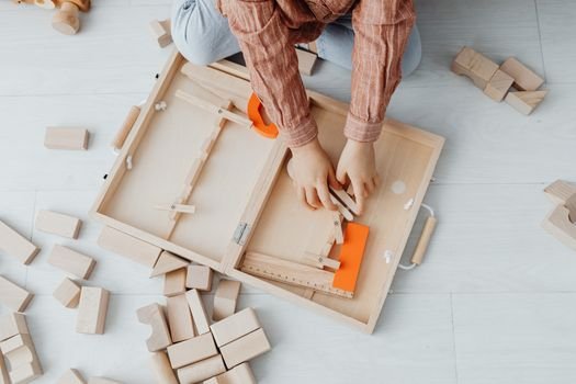 A child playing with wooden blocks and a toy set on a light floor, fostering creativity and fun.