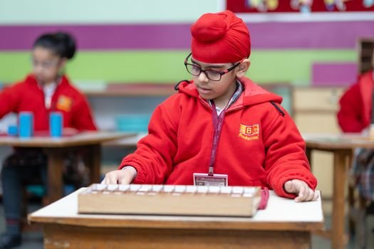 A child in a Montessori school setting focusing on an educational task, wearing a red turban and jacket.