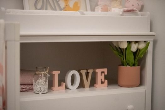 Charming shelf decor featuring white tulips, a LOVE sign, and soft pastels in a cozy nursery setting.