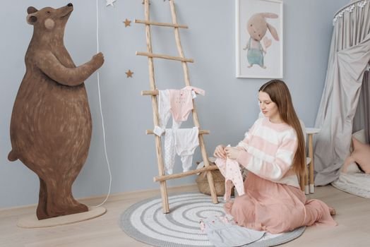 A pregnant woman sits on the floor folding baby clothes in a beautifully decorated nursery.