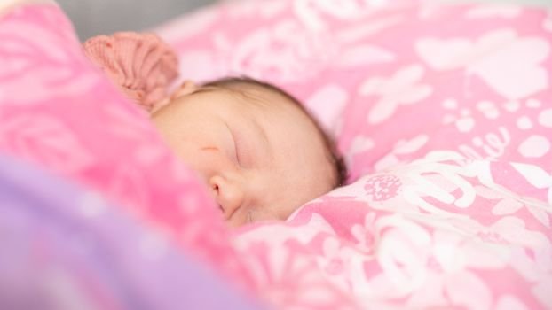 A serene portrait of a sleeping baby nestled on a pink-patterned pillow, capturing tranquility.
