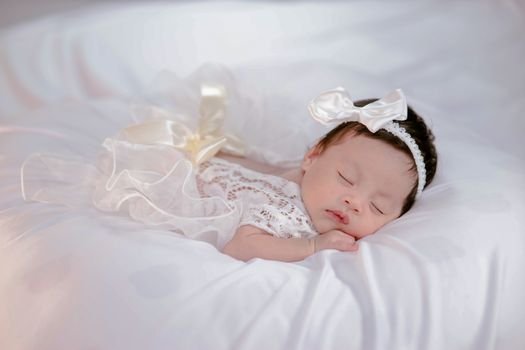 Peaceful sleeping newborn wearing white lace and bow, lying on soft bedding. Capturing the serenity and innocence of infancy.