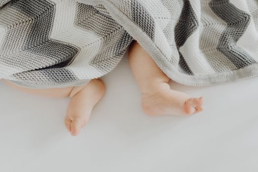Charming view of a baby's feet under a cozy patterned blanket.