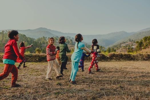 Joyful group of kids playing in a scenic mountain field in Uttarakhand, India at daytime.