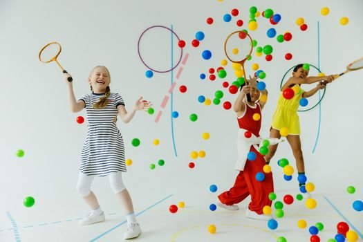 Children playing indoors with rackets and colorful balls, showcasing joy and diversity.