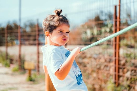 A young boy playing outdoors with a blue rope, enjoying a sunny day.