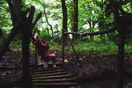 A young girl navigates a rustic bridge in a lush forest setting, capturing adventure and exploration.