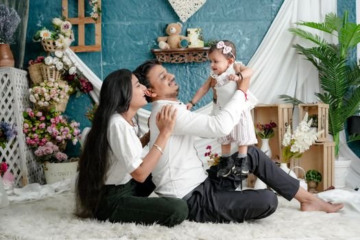 A joyful family moment indoors with parents and baby surrounded by flowers.