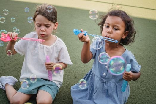 Two young girls enjoy a playful summer day blowing bubbles outdoors on a grassy field.