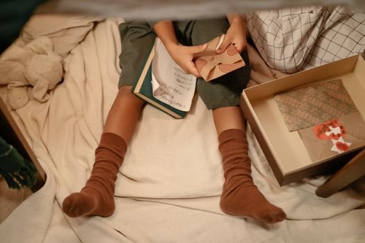 Child sitting under blanket sorting greeting cards, cozy setting indoors.