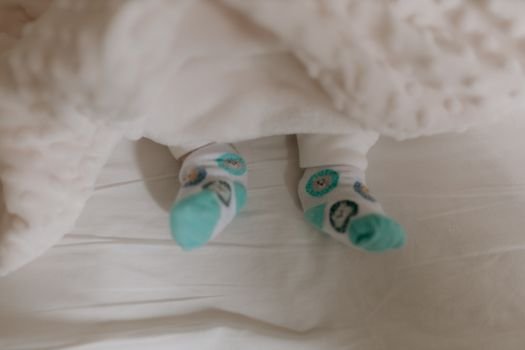 Adorable baby feet wearing cute patterned socks, nestled under a soft white blanket.