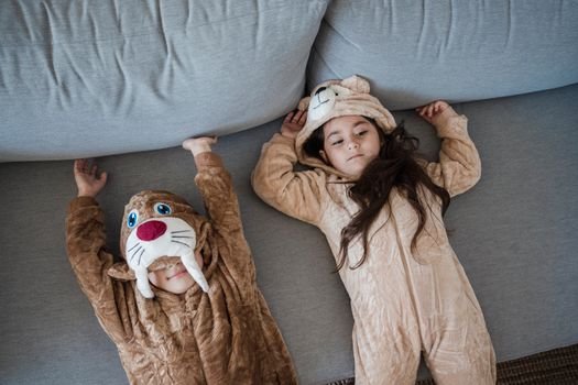 Two kids in cozy animal onesies lying on a comfortable sofa.