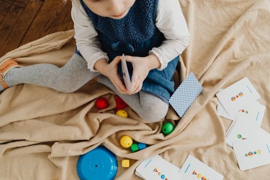 A young girl engaged with colorful educational flash cards and toys on a mat indoors.